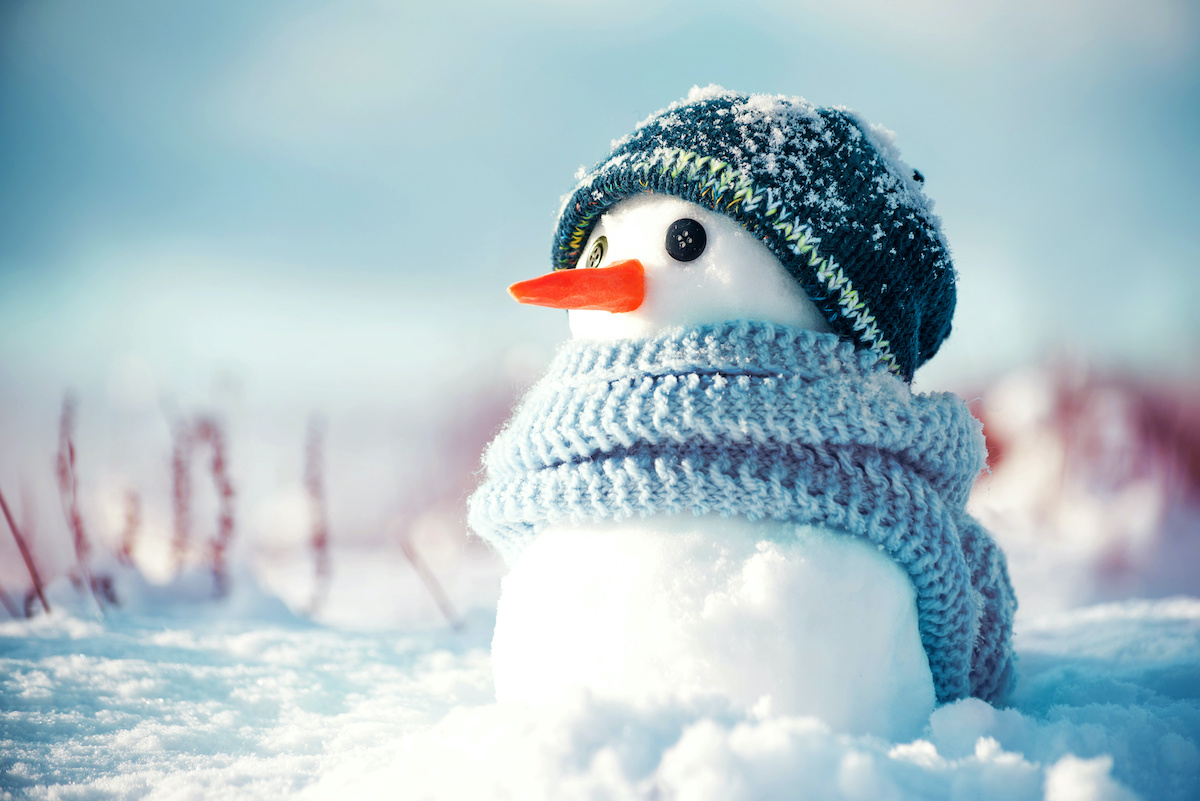 Little cute snowman in a knitted hat and scarf on snow on a sunny winter day. Christmas card